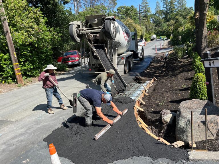A civil works construction crew pouring and leveling fresh paving material from a mixer truck for a public agency road repair project.