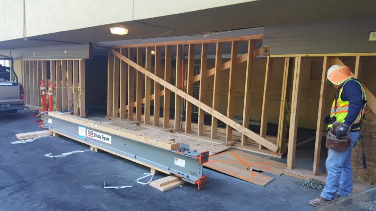 A commercial construction contractor preparing to install a large structural steel beam and wood wall framing for a building reinforcement project.